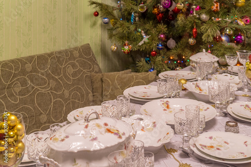 Served table with festive tableware near beautiful decorated Christmas tree in living room interior. Concept of new year holiday at cozy home
