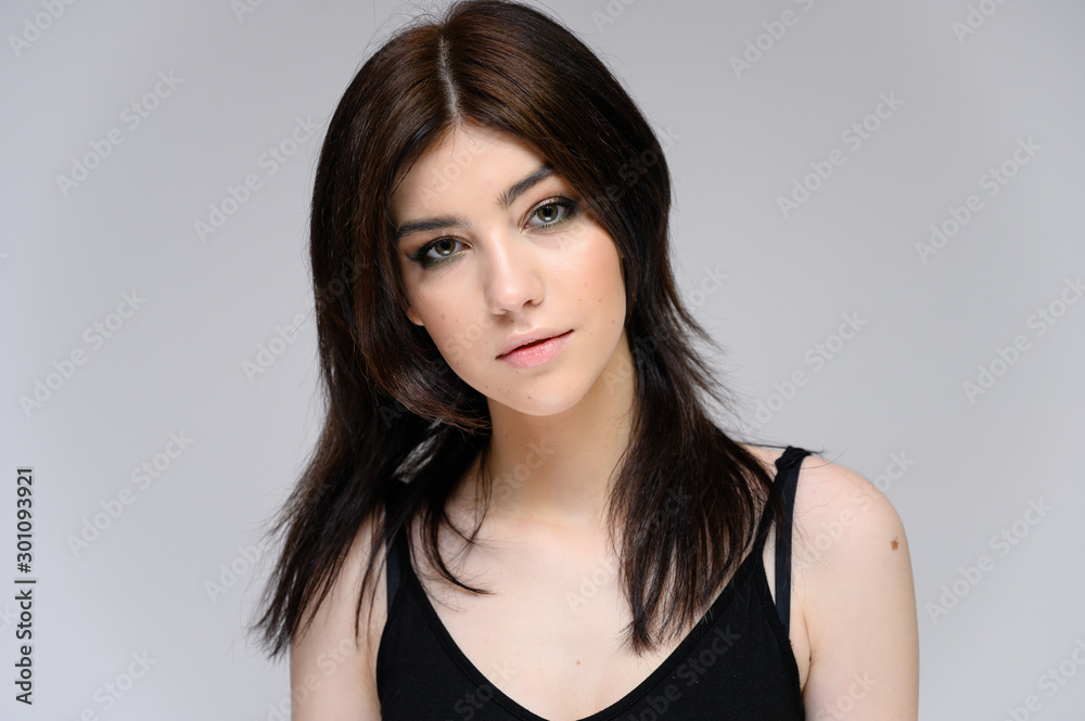 Close-up portrait of a young pretty girl with long black hair, clean skin on a gray background. The concept of cosmetics for the face, great makeup, fashionable hairstyle. Close-up portrait of a young pretty girl with long black hair, clean skin on a gray background. The concept of cosmetics for the face, great makeup, fashionable hairstyle.