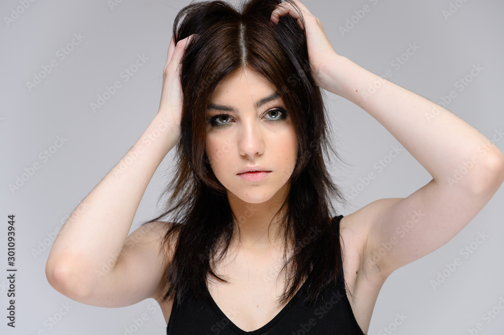 Fototapeta premium Close-up portrait of a young pretty girl with long black hair, clean skin on a gray background. The concept of cosmetics for the face, great makeup, fashionable hairstyle.