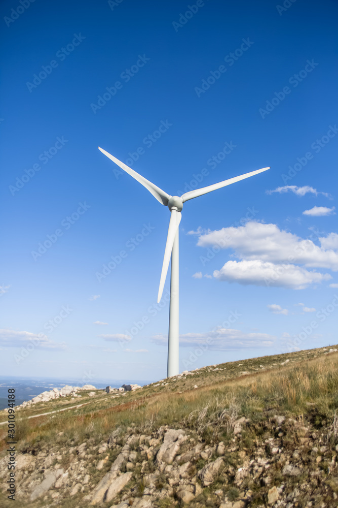 View of a wind turbine on top of mountains, blue sky as background View of a wind turbine on top of mountains, blue sky as background