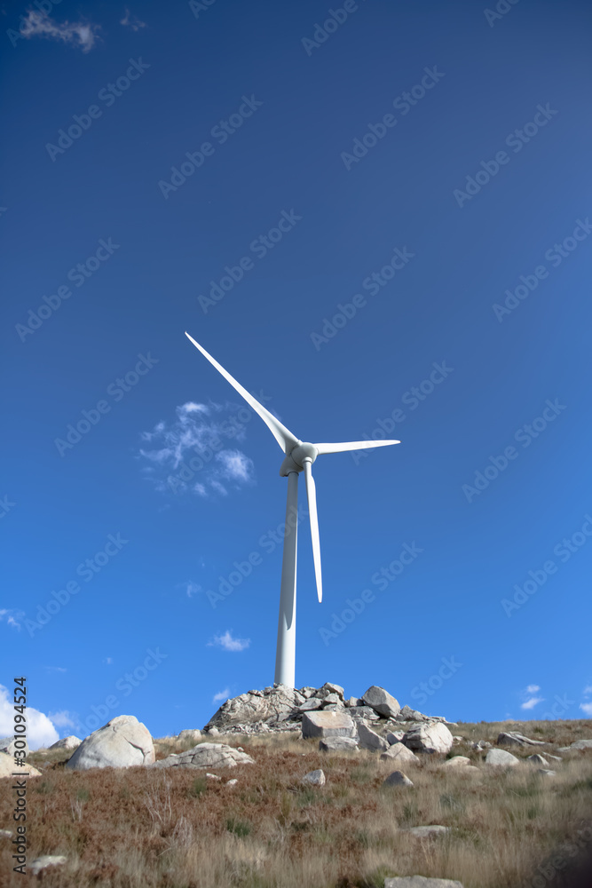 View of a wind turbine on top of mountains, blue sky as background View of a wind turbine on top of mountains, blue sky as background