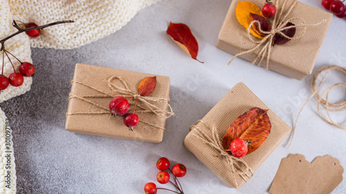 Autumn vibes, thanksgiving day presents, seasonal sale concept. Fall composition with presents in craft paper decorated with dried leaves and red berries on gray background. Top view
