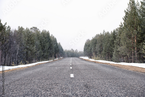 The lonely road in the forest with the falling snow