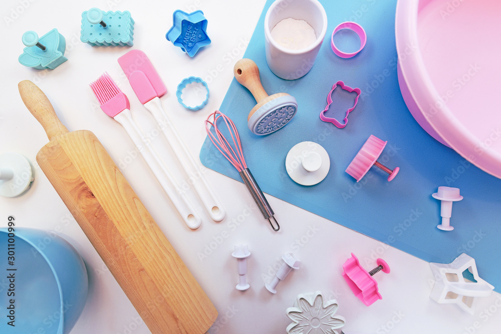 Top view flat lay with cute pink and blue baking utensils like baking mat, wooden rolling pin, mixing bowls and cookie cutters on white background Top view flat lay with cute pink and blue baking utensils like baking mat, wooden rolling pin, mixing bowls and cookie cutters on white background