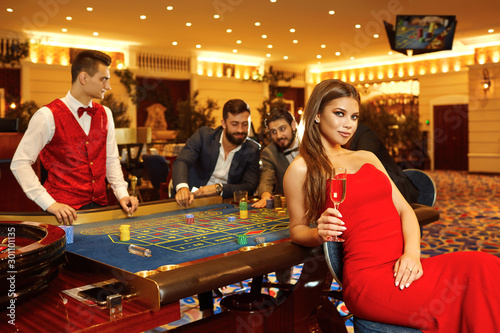 A woman with glass of champagne in a dress at table roulette in casino.
