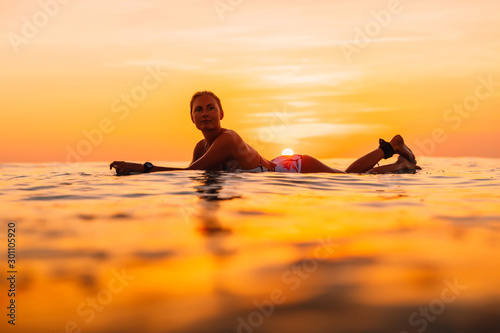 Attractive surfer woman on a surfboard in ocean. Surfgirl at sunset