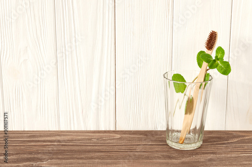 bamboo toothbrush in the glass, with mint on light brown and white wooden background. zero waste lifestyle