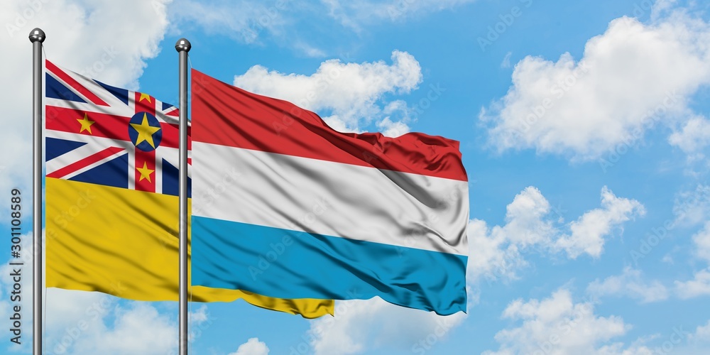 Niue and Luxembourg flag waving in the wind against white cloudy blue sky together. Diplomacy concept, international relations.