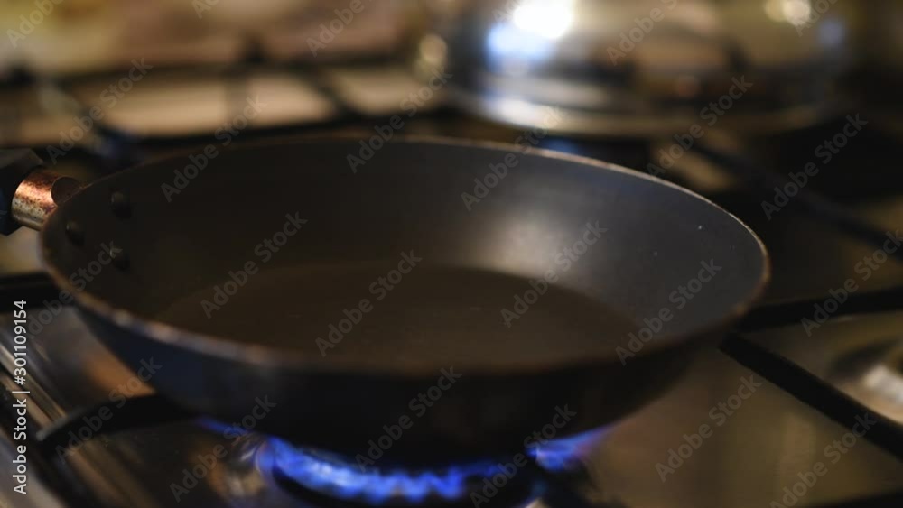 Process of heating frying pan on gas stove. Hand pours oil into a hot pan Process of heating frying pan on gas stove. Hand pours oil into a hot pan