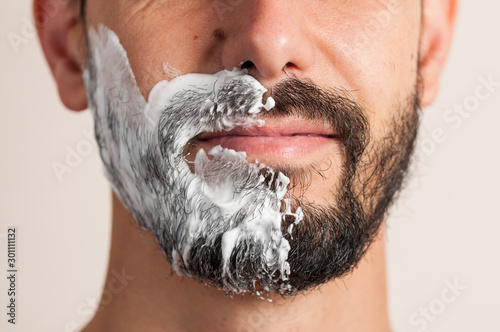 Macro photo man is shaving beard. Beard shaving procedure.Foam and shaver