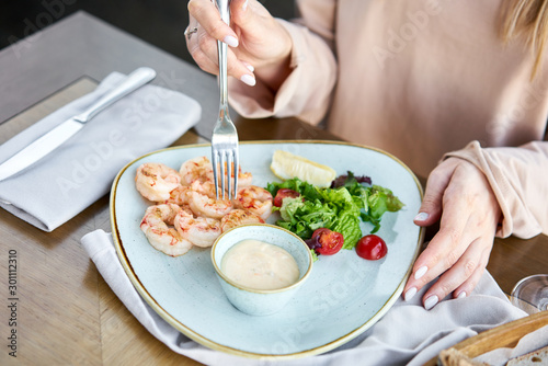Grilled Argentine shrimp with mango-jalapeno sauce. Lunch in a restaurant, a woman eats delicious and healthy food. Delicious fresh seafood prawns with fresh vegetables and lime. Cream sauce