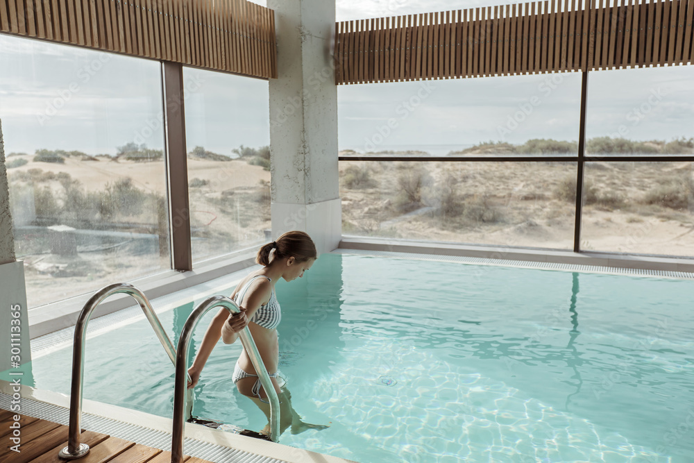 Girl relaxing in luxury swimming pool in modern hotel - obrazy, fototapety, plakaty 