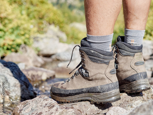 Close up view of high trekking boots and male legs on stony mountain top; dangerous hiking route with professional reliable equipment