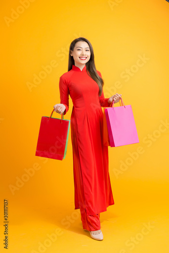 Vietnamese woman wearing traditional ao dai clothes and holding shopping bags in Tet festival on white background