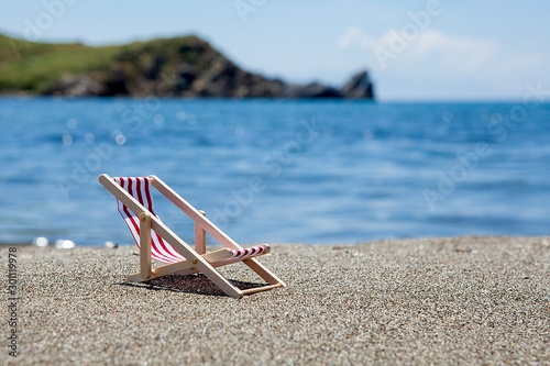 Toy chaise longue on sandy beach on sunny day at the blue sea background. Relaxation concept.