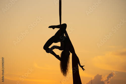 Silhouette of a flexible woman acrobat on aerial silk during a sunset. concept beauty