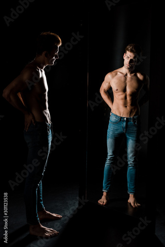 handsome shirtless man posing in front of mirror in dark room