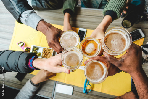Group of friends enjoying a beer glasses in english pub restaurant - Young people cheering at vintage bar - Friendship, happy hour and party concept - Main focus on right half pint glass