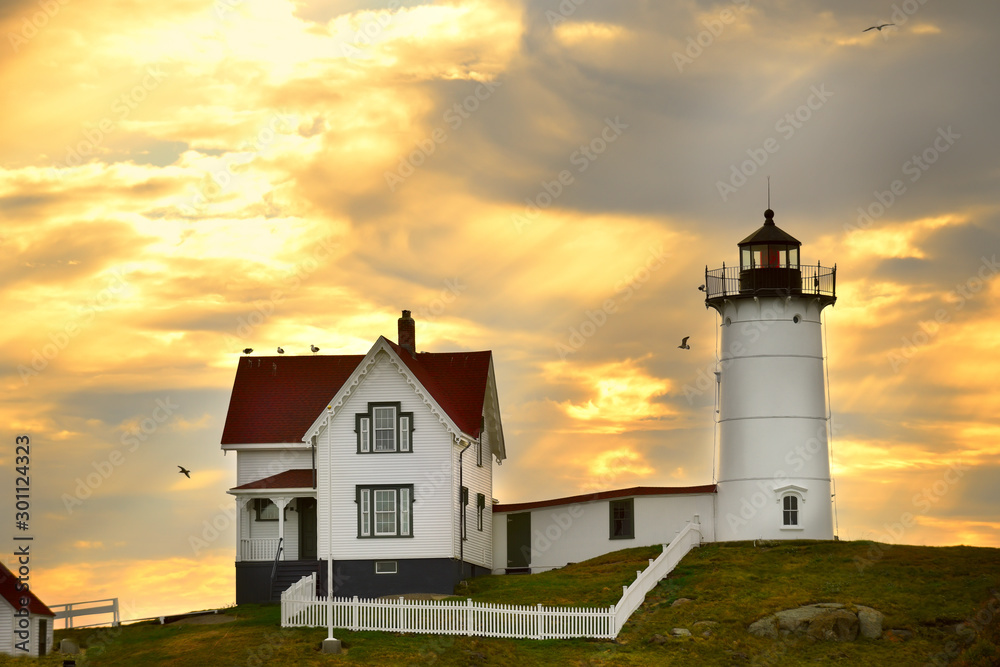 The lighthouse and the house of the keeper of the lighthouse on the hill against the sunset sky. Atlantic Ocean. USA. Maine. Nubble york The lighthouse and the house of the keeper of the lighthouse on the hill against the sunset sky. Atlantic Ocean. USA. Maine. Nubble york