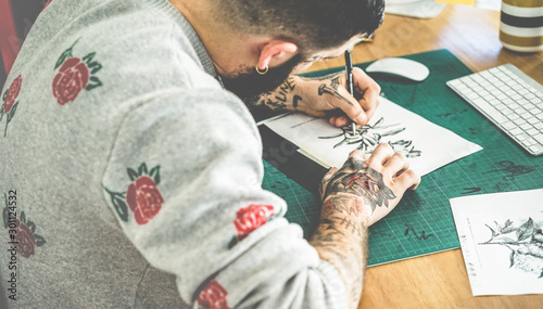 Young tattoo artist drawing sketch inside ink studio - Hipster tattoer at work - Contemporary skin trends generation - Focus on man right hand