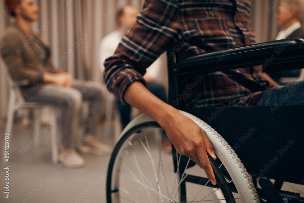 Close-up of young man sitting in wheelchair with group of people in the background Close-up of young man sitting in wheelchair with group of people in the background