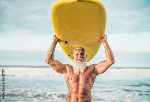 Senior trendy man doing surf with longboard - Happy old guy having fun doing extreme sport - Joyful elderly concept - Focus on his face