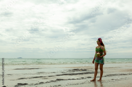 asian girls hold coconut beach walks on vacations, turquoise sea, bright sky and white clouds (concept travel holliday)