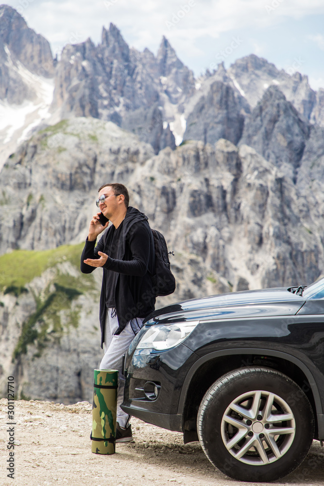 Young handsome man standing near his car and talking on the phone on mountains background