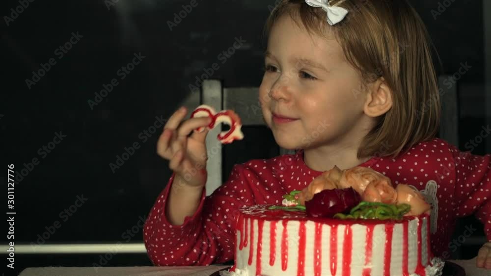 Portrait of little 3 year old smiling child girl celebrates birthday with festive cake with cream, candles, laughs and eats sweet figure 3 from white chocolate with pleasure Portrait of little 3 year old smiling child girl celebrates birthday with festive cake with cream, candles, laughs and eats sweet figure 3 from white chocolate with pleasure