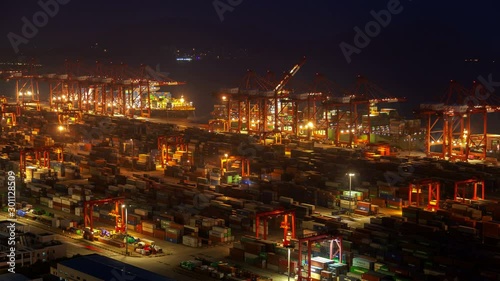 Timelapse illuminated Shanghai cranes load large cargo vessels in Yangshan Port of Shengsi against Chinese hills silhouettes at night photo