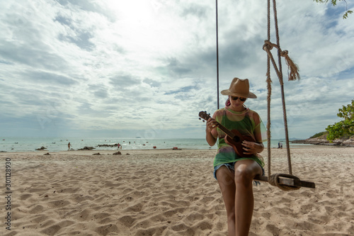 asian girls play ukulele on the beach with the sea and mountains surrounded on weekend