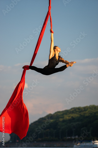 Beautiful and flexible female circus artist dancing with aerial silk on a sky background