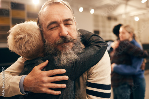 Senior bearded man embracing woman and enjoying the hug during therapy with other couple in the background photo