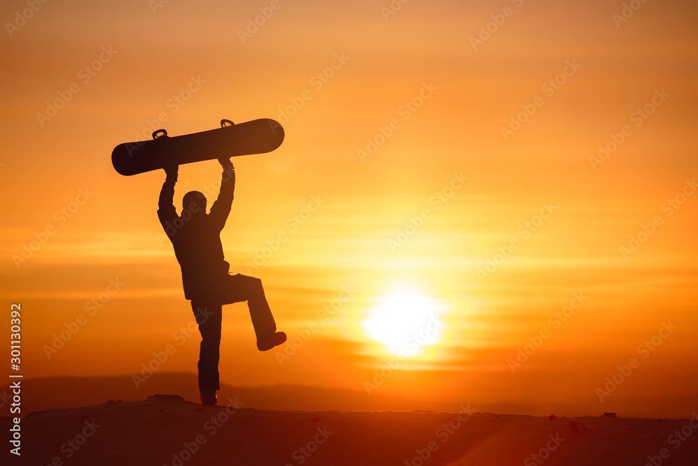 Happy snowboarder dancing with snowboard against sunset
