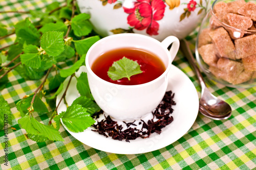 Black tea in a white cup, ceramic teapot, vase of brown sugar with fresh natural birch branches on textile background.