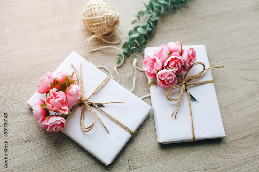 Handmade present box wrapped in paper with branch of roses. Eucalyptus branch and rustic hemp cord spools on background Handmade present box wrapped in paper with branch of roses. Eucalyptus branch and rustic hemp cord spools on background