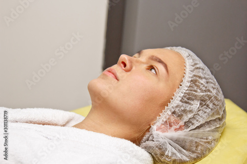 Preparation for procedures in the cosmetologist s office. Beautician in gloves, putting on a hat.