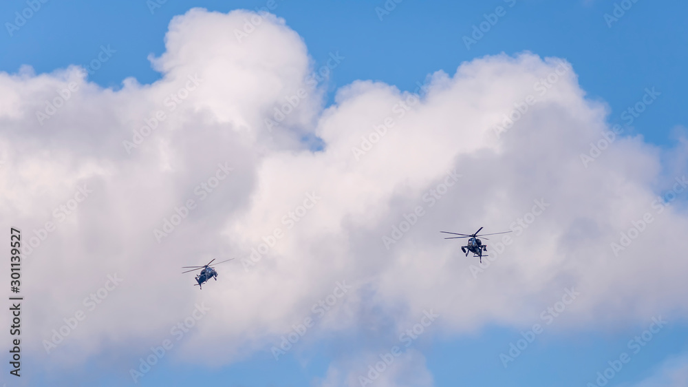 Two military helicopters flying against a beautiful sky with clouds