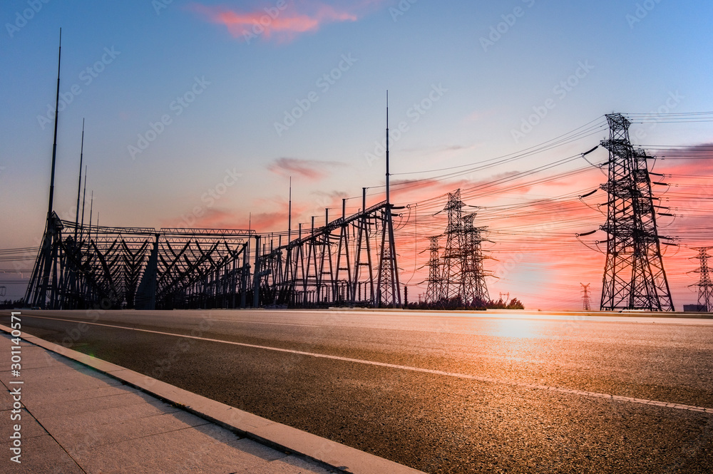 Transmission tower on asphalt road in the setting sun
