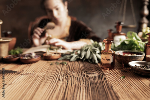 Natural medicine concept. Vintage pharmacist preparing natural medicament. Brass mortar and  bottles. Rustic table. Assorted dry herbs in bowls.