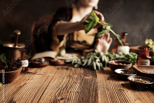 Natural medicine concept. Vintage pharmacist preparing natural medicament. Brass mortar and bottles. Rustic table. Assorted dry herbs in bowls.