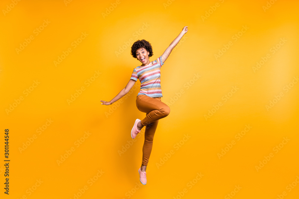Full length body size photo of cheerful positive funky ecstatic overjoyed girl in orange pants striped t-shirt footwear jumping isolated vibrant color background