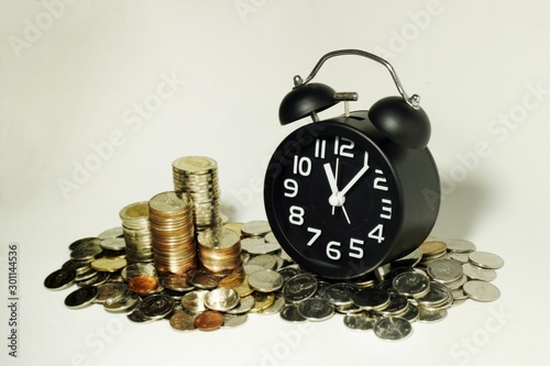 A pile of coins and alarm clock showing income from investment increasing every minute.