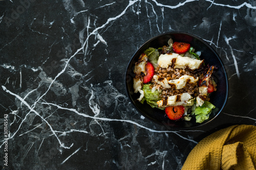 Grilled Halloumi Cheese Salad with Strawberry Slices and Buckwheat / Hellim in Black Bowl on Dark Granite Surface.