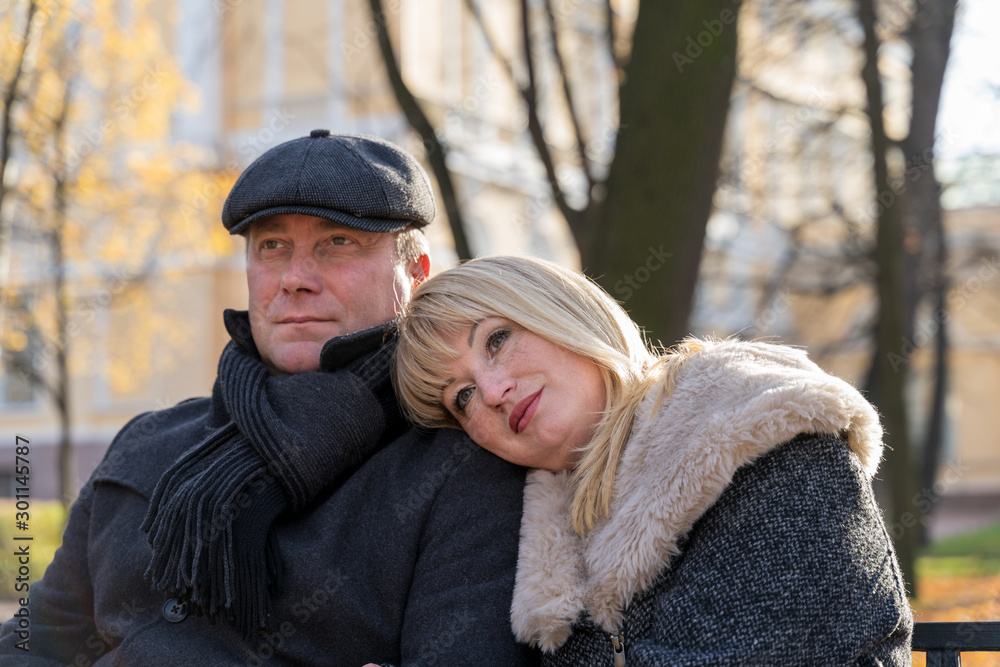 Closeup portrait of happy blonde mature woman and beautiful middle-aged brunette, looking away. Loving couple of 45-50 years old walks in autumn park in warm clothes, in coat and enjoys life