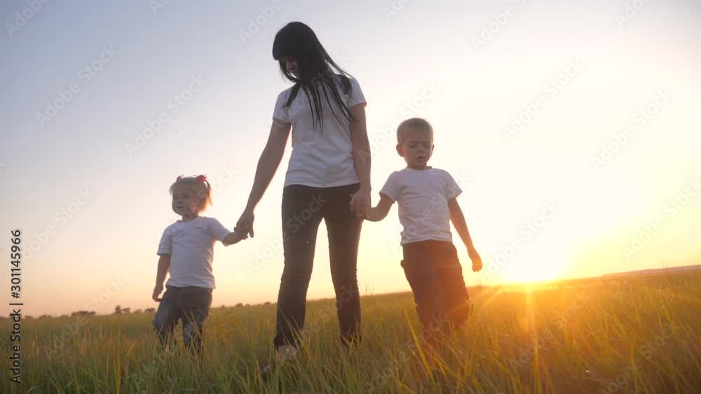 happy family teamwork brother and sister mother hold hands walk in the park lifestyle at sunset on the grass. mother and children slow motion video little girl and boy kids walking in nature outdoors happy family teamwork brother and sister mother hold hands walk in the park lifestyle at sunset on the grass. mother and children slow motion video little girl and boy kids walking in nature outdoors