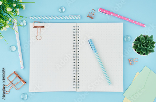 Blank notepad page in bullet journal on bright blue office desktop. Top view of modern table with notebook, stationery. Mock up, copy space, concept for diary