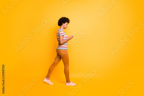 Full length body size photo of pensive concentrated focused girl browsing through social media wearing orange pants trousers footwear walking isolated over vivid color background