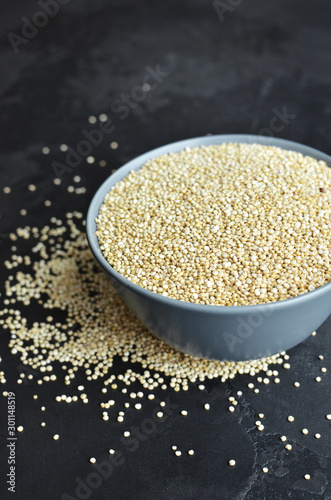 Dry quinoa seed grain in ceramic plate over black grange background