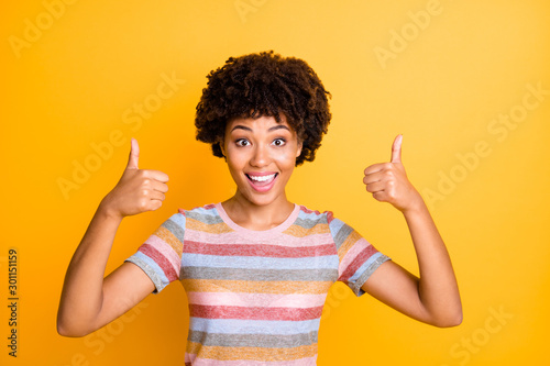 Photo of beautiful dark skin lady holding thumbs raised air expressing agreement and positive attitude wear casual striped t-shirt isolated yellow background photo